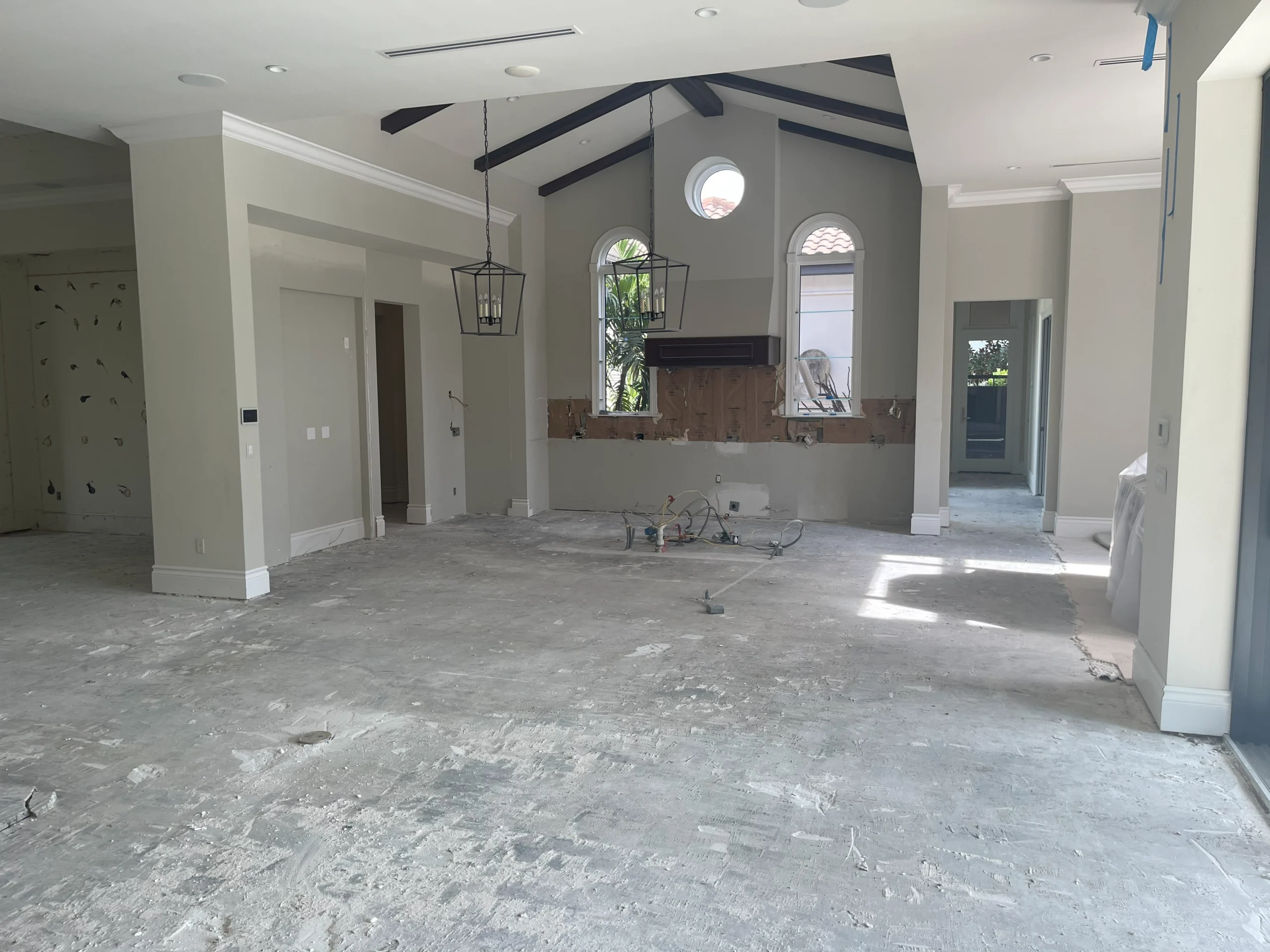 Open room under active renovation — exposed subfloor, vaulted ceiling with dark beams, arched windows visible