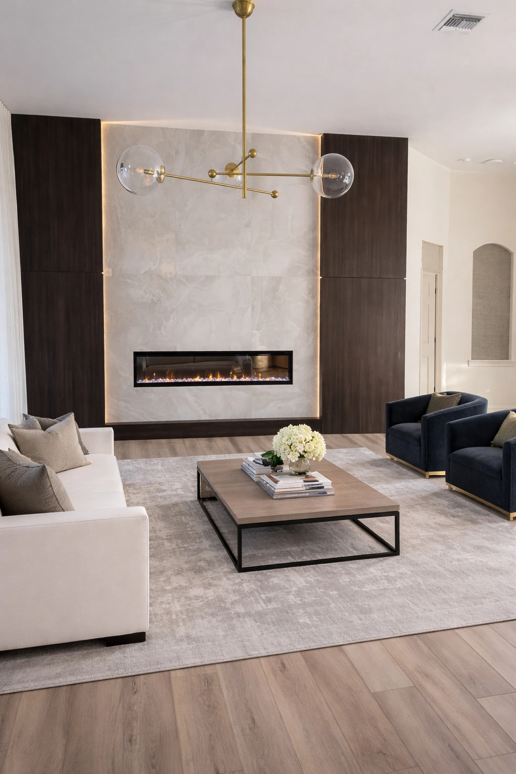 Contemporary living room — wood/stone fireplace wall, gold chandelier, navy accent chairs